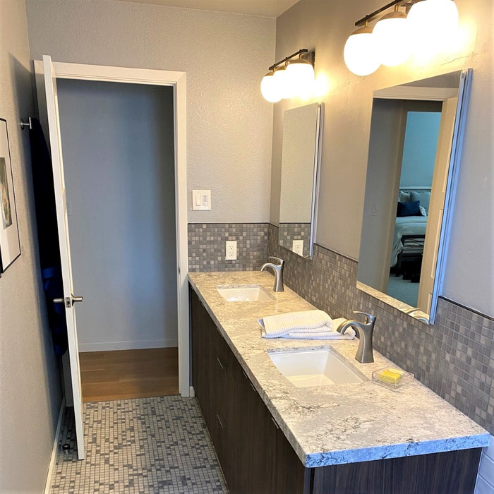 A modern double sink bathroom with granite counters and two different blends of porcelain Mediterranean mosaic tile in light and dark greys for the floor and backsplash. The beautiful German made tiles are perfect for floors, showers, pools & kitchens