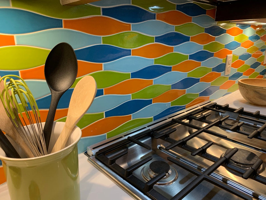 Ceramic minnow shaped tile in bright green, orange and sky blue jazz up this kitchen backsplash, accented by stainless steel appliances, bright ceramic jars and wooden bowls.