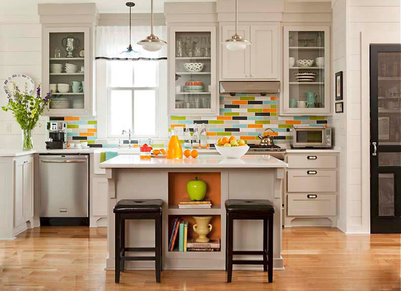 Modern white kitchen with colorful backsplash and wooden floor. Black accents. Kiln handmade ceramic in colors orange green, gray, black, light blue, and tan.